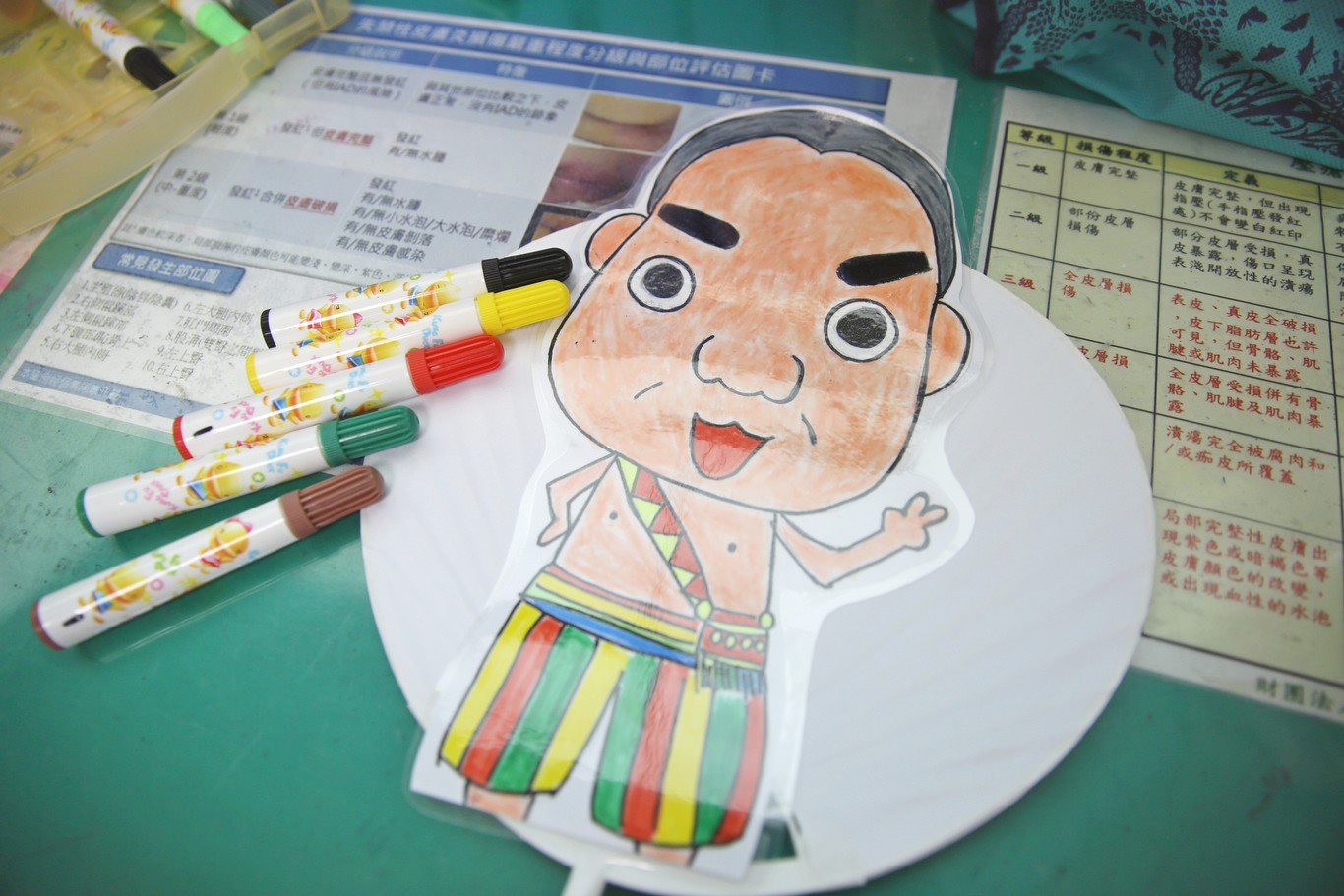 照護陳阿公的輕症病房護理師們繪製有著阿公畫像的Q版扇子，特別畫上阿美族族服代表勇士，祝福阿公平安出院。