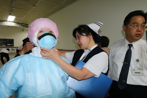 鍾惠君（中）致力院內推動感染管制專業及各項防疫業務推動。護理部鍾惠君副主任在門診、病房病患舉辦「因應伊波拉病毒感染門住院病患轉送演練」中，擔任考評官檢視清潔人員的防護衣穿脫流程步驟是否皆正確執行