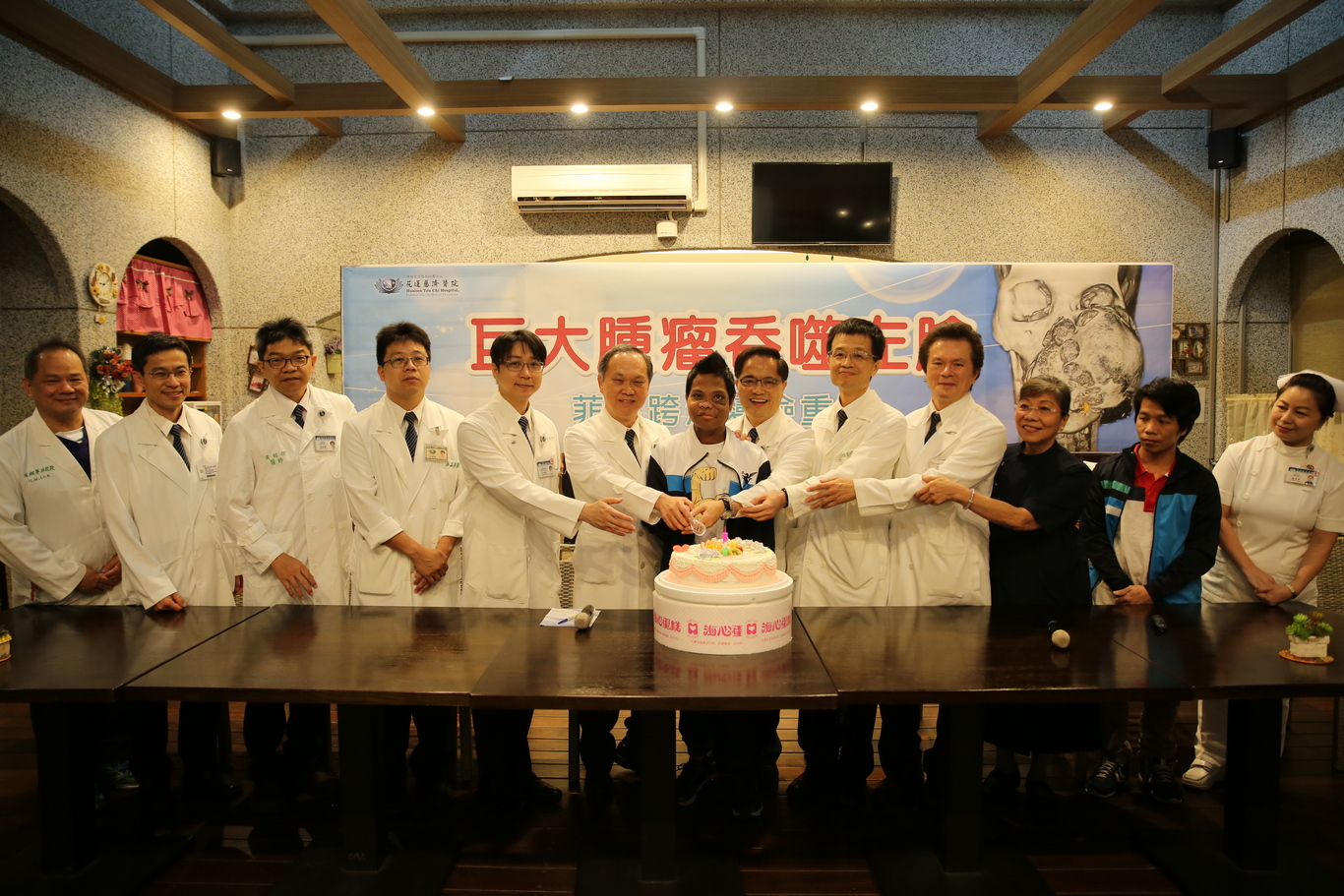 花蓮慈院林欣榮院長(右六)、陳培榕副院長(右五)、外科醫學發展中心主任賴鴻緒(左六)、外科部主任張睿智(左五)、整形暨重建外科主任李俊達(右四)、吳孟熹醫師(左四)，眼科部主任李原傑(左二)、牙科部主任黃銘傑(左三)、麻醉科主任陸翔寧(左一)，護理部主任鍾惠君(右一)，一起切下蛋糕，祝福麥可變臉成功歡喜出院